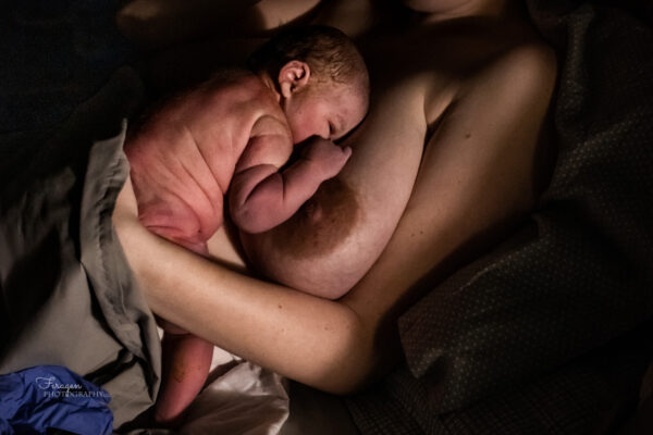 Newborn resting with eyes open upon Mother's bare chest.