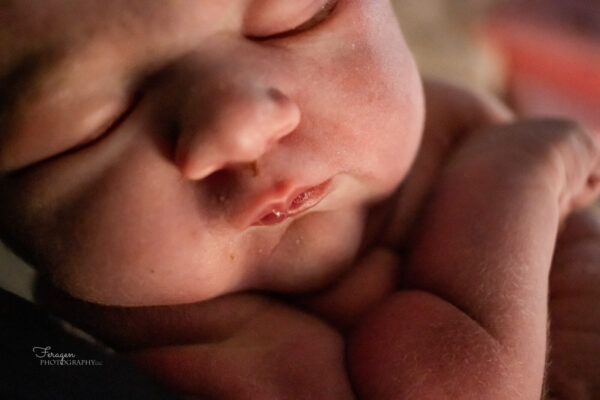 Close up photo of newborn's face and arm.  Baby is sleeping peacefully.