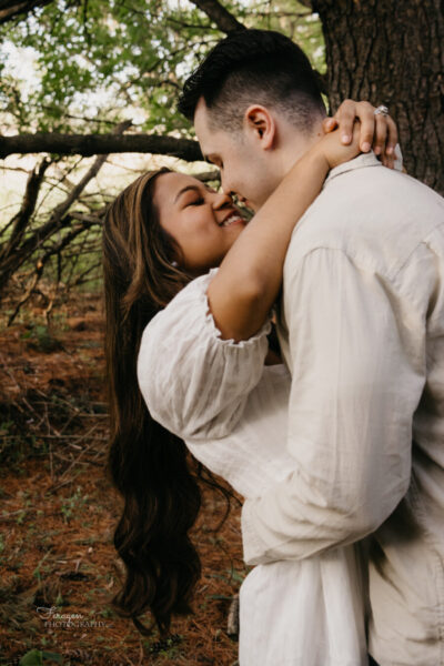 Engaged couple embraces in forest background.